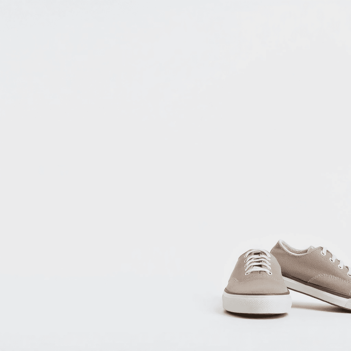 Gambar close-up dari kain kanvas katun yang dipintal rapat di samping sepatu kanvas kasual berwarna netral di latar belakang yang bersih dan minima...