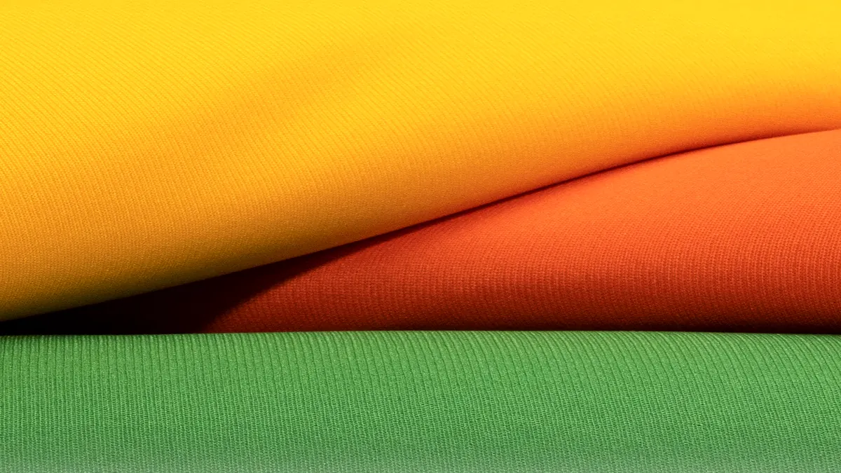 Tumpukan kain hyget Nomitex warna kuning, oranye, dan hijau dari dekat, tampak tekstur rajutannya